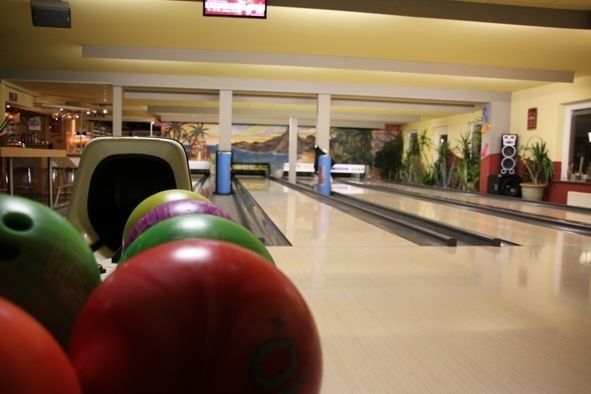 Bowlingkugeln vor mehreren glänzenden Bahnen in einer Bowlinghalle